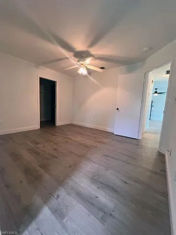 Unfurnished bedroom featuring dark wood-style floors, a spacious closet, and ceiling fan