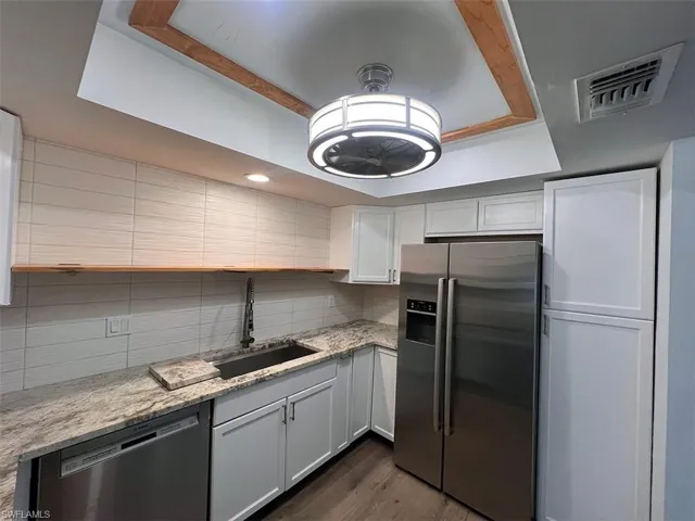 Kitchen featuring stainless steel appliances, light stone counters, a tray ceiling, dark wood-style flooring, and white cabinets