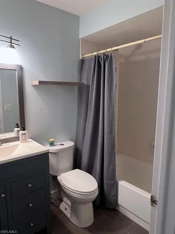 Bathroom with vanity, dark tile patterned floors, and shower / bathtub combination with curtain