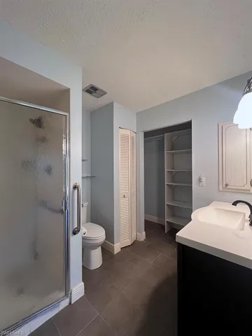 Bathroom with vanity, a stall shower, a textured ceiling, and a spacious closet