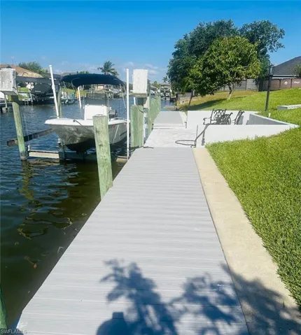 Dock with boat lift, a water view, and a lawn