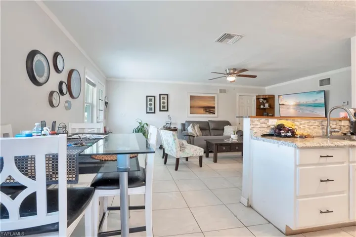 Kitchen featuring white cabinets, ornamental molding, a ceiling fan, light stone counters, and light tile patterned flooring