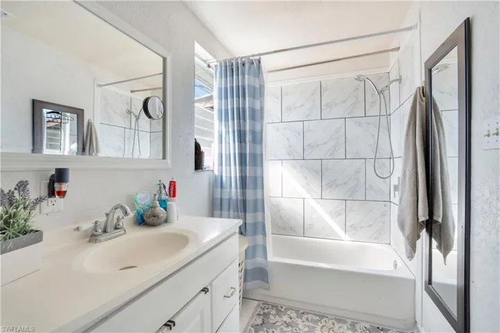 Bathroom featuring vanity, shower / tub combo with curtain, and a textured wall