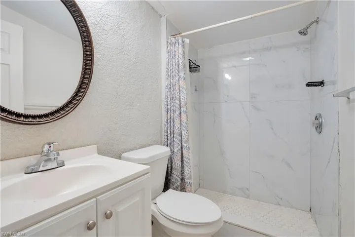 Full bathroom featuring a textured wall, vanity, and a marble finish shower