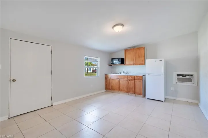 Kitchen featuring light countertops, freestanding refrigerator, wood finish cabinets, black microwave, and light tile patterned floors