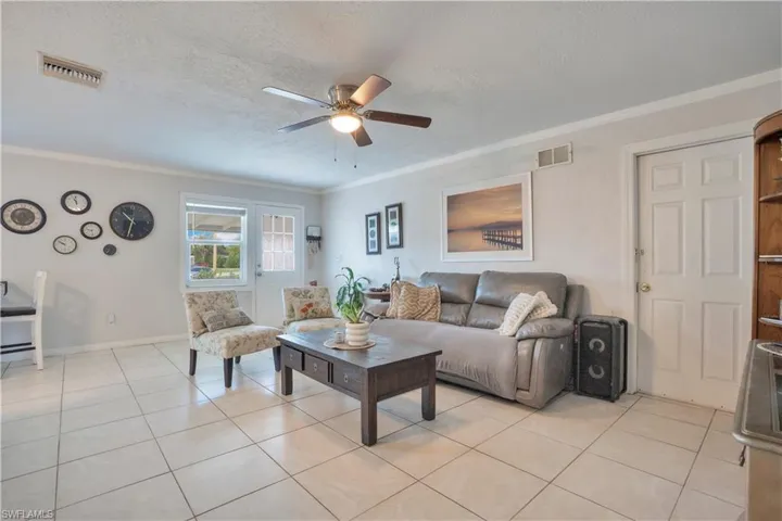 Living area with ceiling fan, light tile patterned floors, a textured ceiling, and ornamental molding
