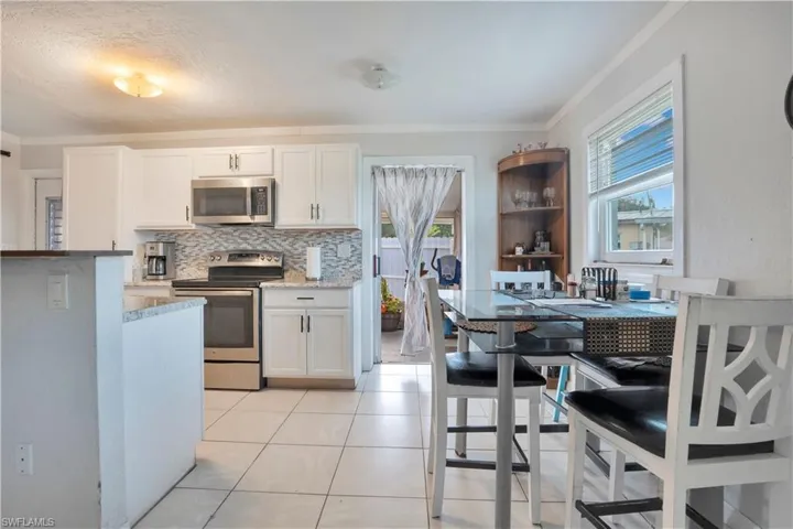 Kitchen featuring stainless steel appliances, white cabinetry, tasteful backsplash, light tile patterned floors, and light stone countertops