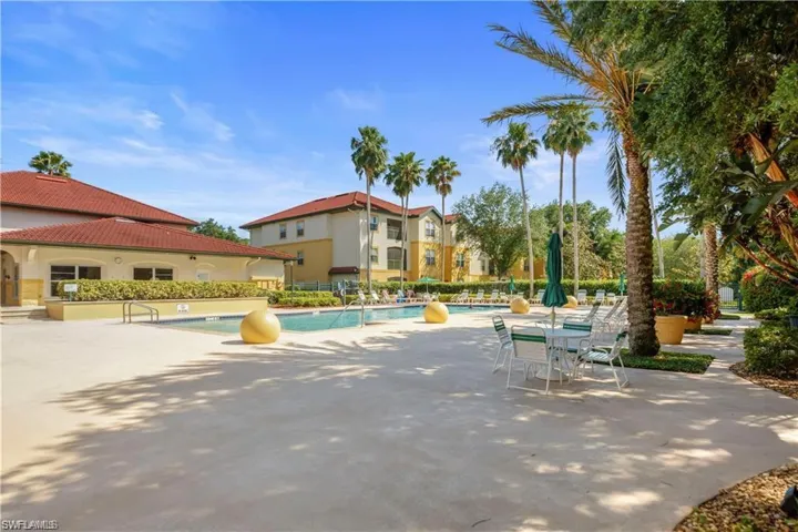 Resort-style pool area featuring a large swimming pool, expansive concrete decking, and mature palm trees