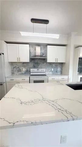 Kitchen featuring a white quartz-finish island countertop, white cabinetry with gold-tone hardware, and a patterned backsplash