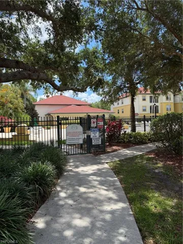 Paved walkway leading to a gated entry with black wrought iron fencing
