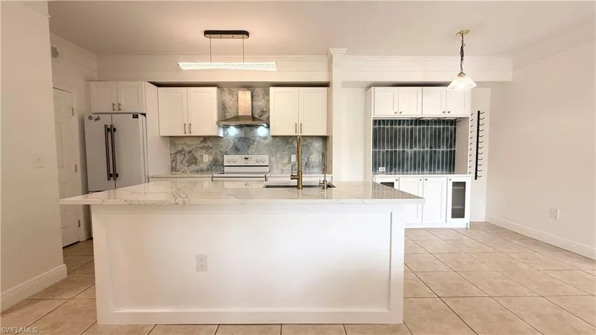 Kitchen featuring a central island with a light-colored countertop, white cabinetry, a stainless steel range hood, and tile flooring