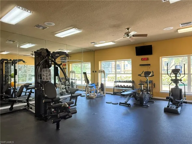 Fitness center featuring rubber flooring, mirrored wall, large windows, ceiling fan, and mounted television