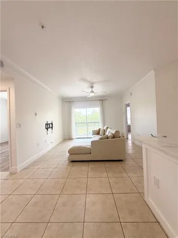 Spacious living area featuring neutral tile flooring, crown molding, and a ceiling fan