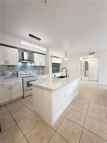 Modern kitchen featuring a large central island with a waterfall countertop, white cabinetry, a built-in range hood, and a decorative backsplash