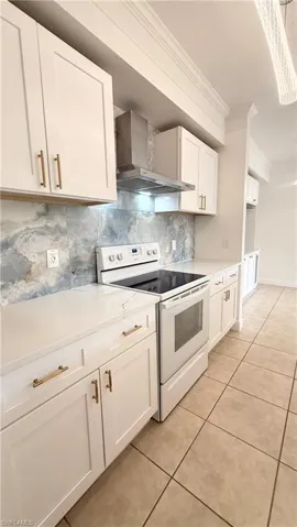 Modern kitchen featuring white shaker cabinetry with gold-toned hardware, solid surface countertops, and a full-height blue and white variegated backsplash