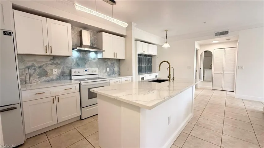 Contemporary kitchen featuring white cabinetry, a large center island with a black sink and brass faucet, white appliances, and a unique blue and white patterned backsplash