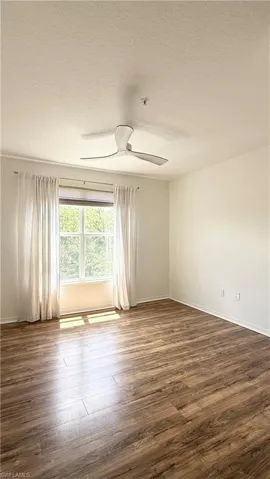 Spacious room featuring wood-finish flooring, a modern ceiling fan, and a large window with privacy blinds