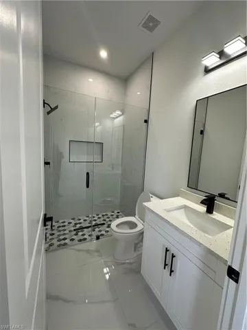 Full bath with visible vents, toilet, marble finish floor, vanity, and a shower stall
