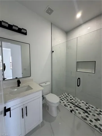 Bathroom with visible vents, toilet, marble finish floor, vanity, and a shower stall
