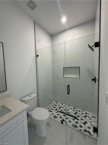 Full bath with toilet, vanity, a shower stall, and visible vents