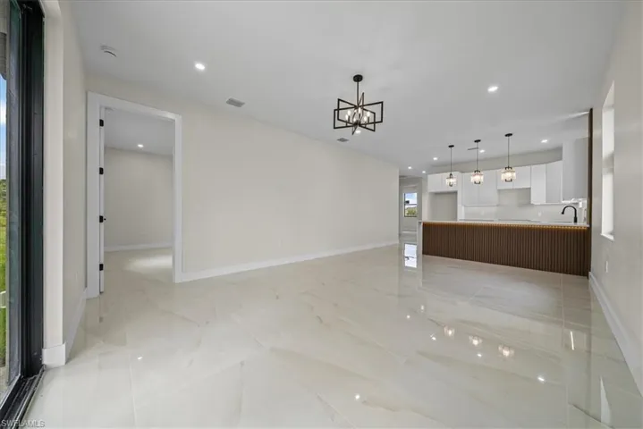 Spacious open-concept living area featuring large format polished tile flooring, recessed lighting, and a contemporary chandelier