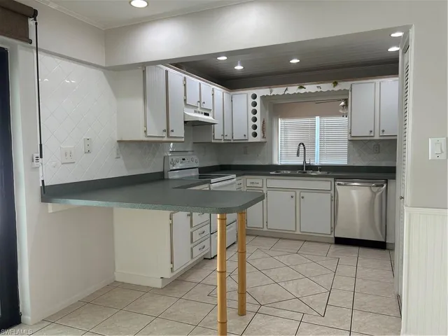 Kitchen featuring dark countertops, dishwasher, range hood, stove, and a sink