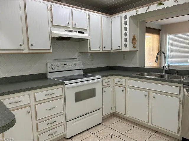 Kitchen with dark countertops, ventilation hood, range, light tile patterned flooring, and a sink