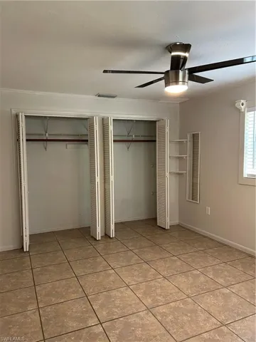 Unfurnished bedroom with light tile patterned flooring, ceiling fan, baseboards, and multiple closets