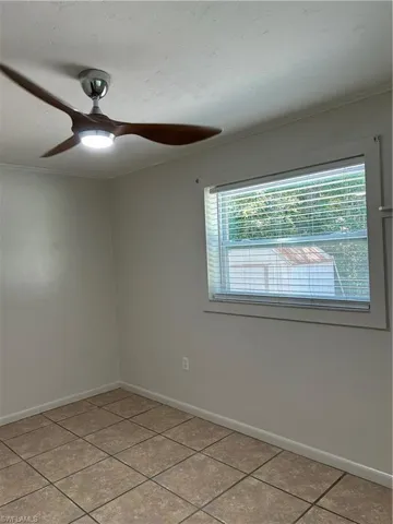 Empty room featuring tile patterned flooring, a ceiling fan, crown molding, and baseboards