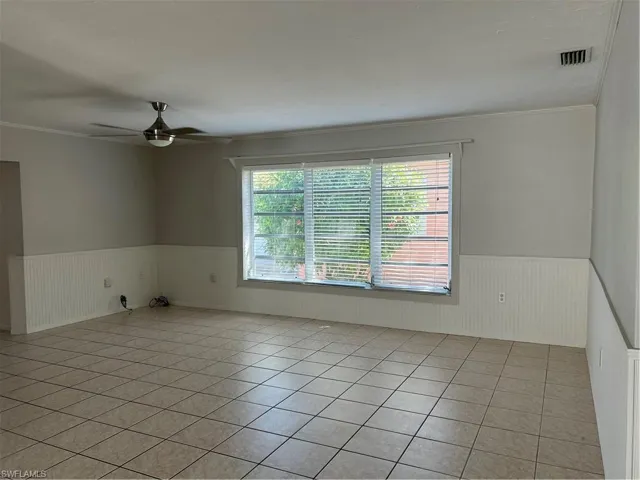 Unfurnished room featuring visible vents, crown molding, wainscoting, light tile patterned flooring, and a ceiling fan