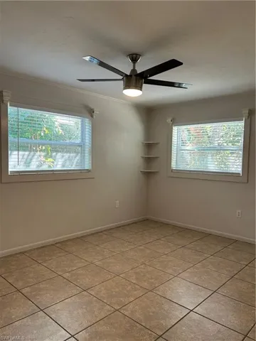 Empty room with crown molding, light tile patterned floors, a ceiling fan, and baseboards