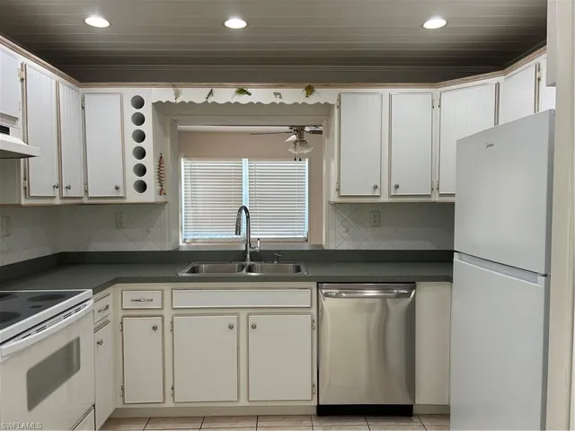 Kitchen featuring dark countertops, a sink, dishwashing machine, refrigerator, and range