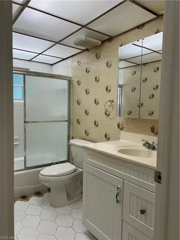 Bathroom with visible vents, toilet, vanity, combined bath / shower with glass door, and tile walls