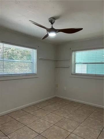 Spare room featuring tile patterned floors, ceiling fan, crown molding, and baseboards