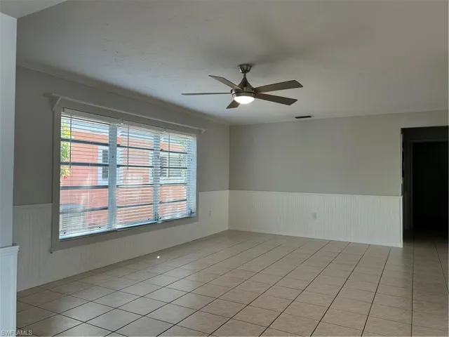 Spare room with light tile patterned floors, a wainscoted wall, visible vents, and ceiling fan