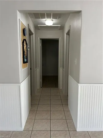 Hall featuring light tile patterned floors, a wainscoted wall, and attic access