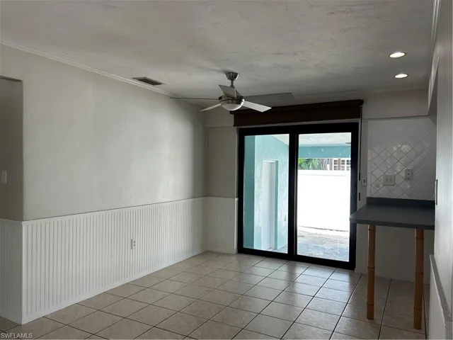 Unfurnished room with visible vents, crown molding, a wainscoted wall, light tile patterned floors, and a ceiling fan