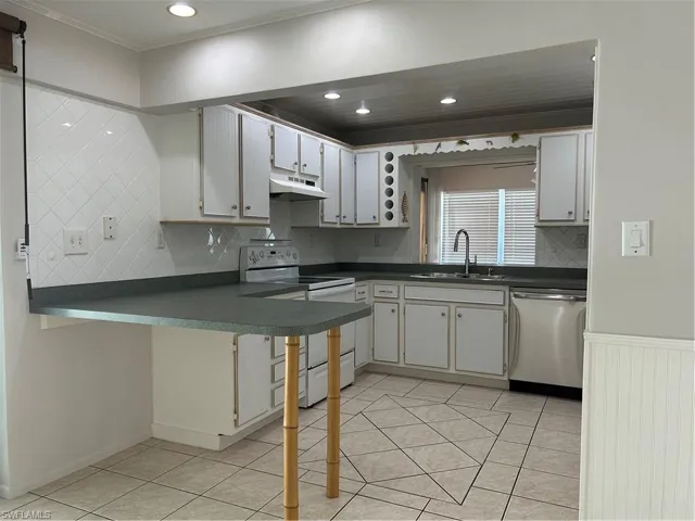 Kitchen featuring range hood, a sink, stove, dishwasher, and dark countertops