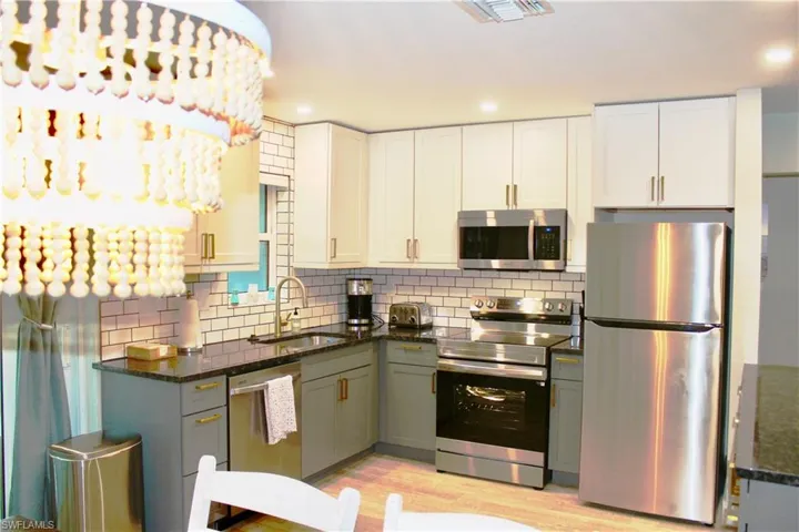 Kitchen with stainless steel appliances, white cabinetry, dark stone countertops, light wood-style flooring, and recessed lighting