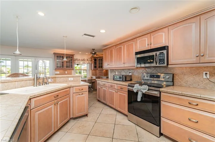 Kitchen featuring stainless steel appliances, glass insert cabinets, tile countertops, backsplash, and recessed lighting