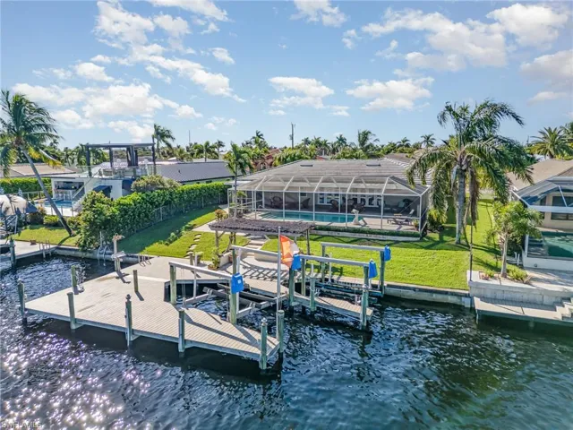 Dock area featuring boat lift, glass enclosure, a lawn, a water view, and an outdoor pool