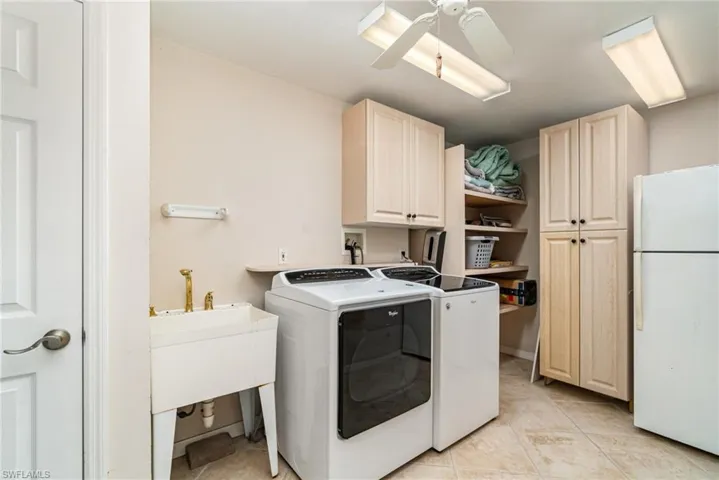 Laundry room with washing machine and clothes dryer, light tile patterned floors, cabinet space, and a ceiling fan
