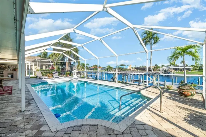 Swimming pool with glass enclosure, a patio, and a water view