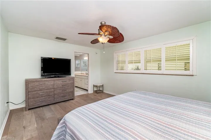 Bedroom with dark wood finished floors, ceiling fan, and ensuite bath