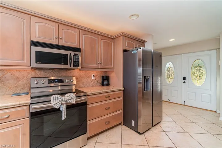 Kitchen with stainless steel appliances, decorative backsplash, light tile patterned floors, and recessed lighting