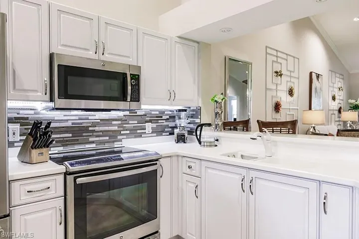 Kitchen featuring white cabinetry, crown molding, appliances with stainless steel finishes, vaulted ceiling, and sink