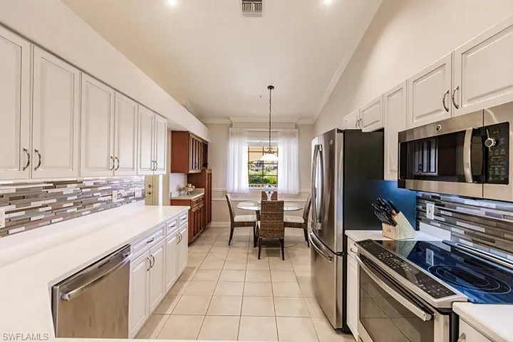 Kitchen with white cabinetry, tasteful backsplash, hanging light fixtures, vaulted ceiling, and appliances with stainless steel finishes