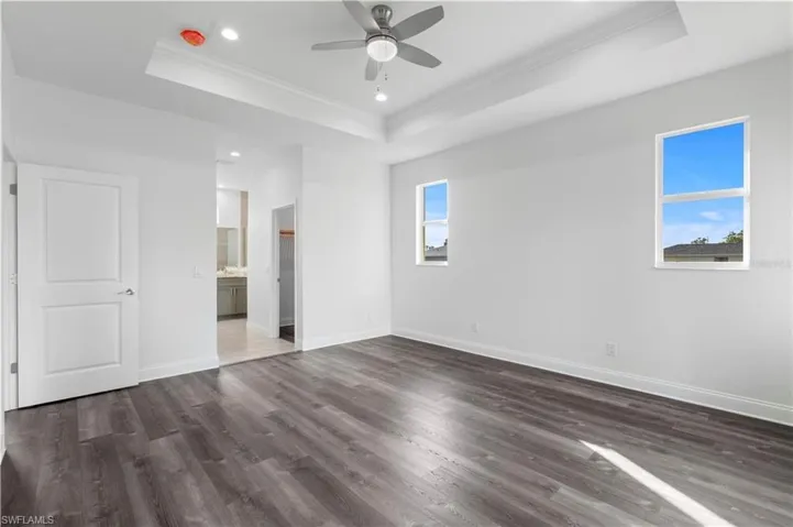Unfurnished bedroom with a tray ceiling, ornamental molding, dark wood-type flooring, baseboards, and recessed lighting