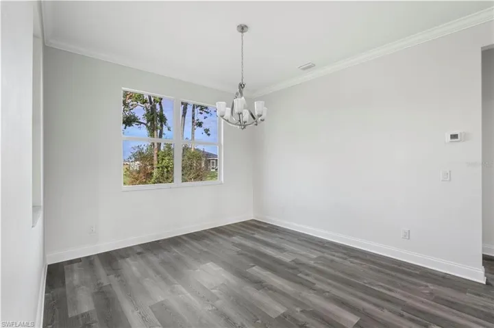 Empty room featuring a chandelier, baseboards, dark wood-style flooring, and ornamental molding