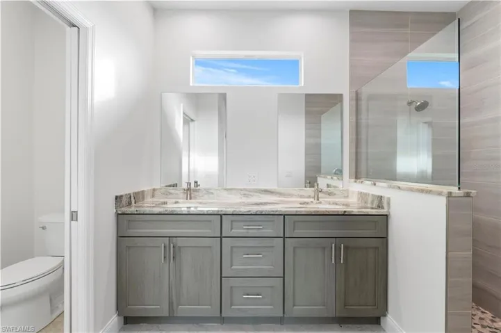 Full bath featuring a walk in shower, double vanity, toilet, and baseboards